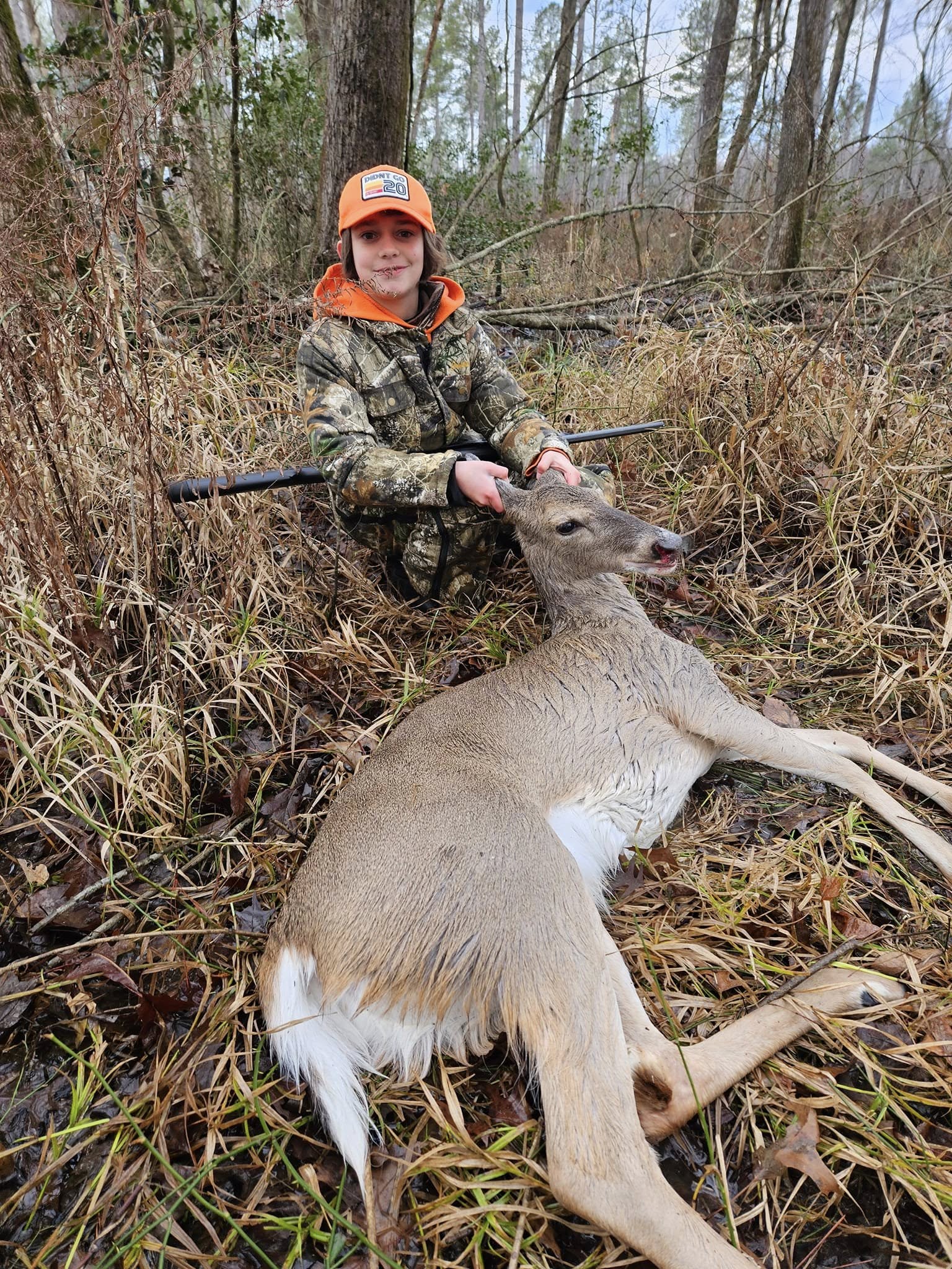 Carter in hunting clothes with a harvested deer in the woods